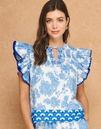 The Berkley Top – blue and white floral print top, ruffle flutter sleeves, tie neck, border print hem